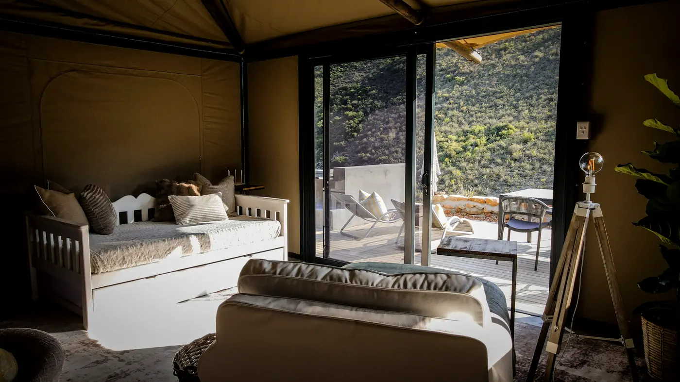 A robe hanging beside the bed, with canvas windows open to the fynbos slopes beyond