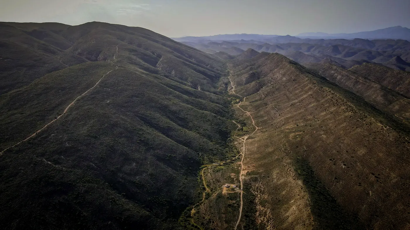 Aerial view of the folded mountains above Montagu, with the farm track winding through the valley toward the tent