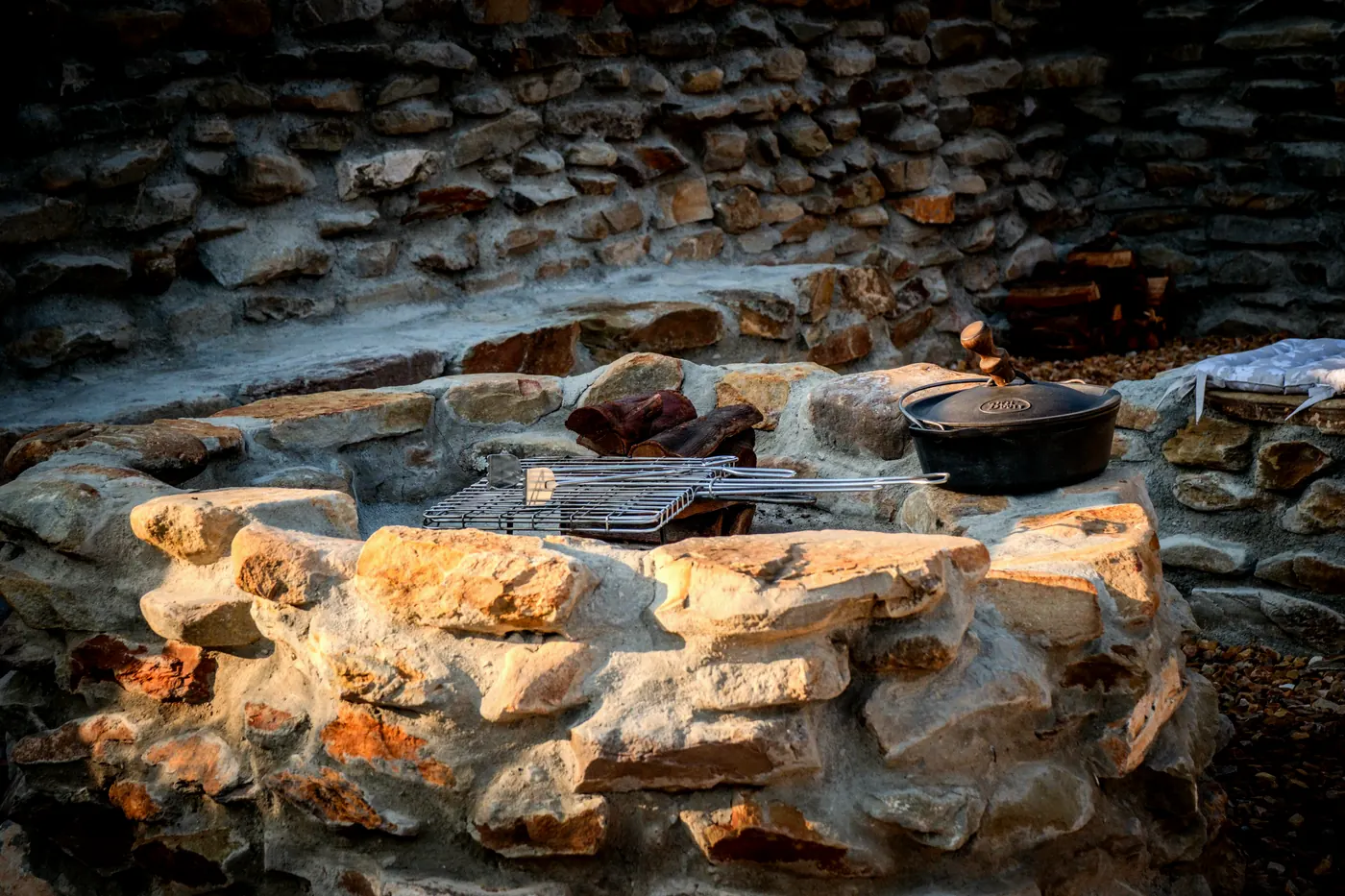 A stone fire pit with a braai grid and cast iron potjie pot, built into a dry packed stone wall
